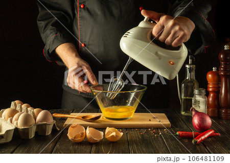 The chef uses a hand-held electric mixer to prepare a delicious egg breakfast or lunch. Menu idea for restaurant or hotel on black background 106481109