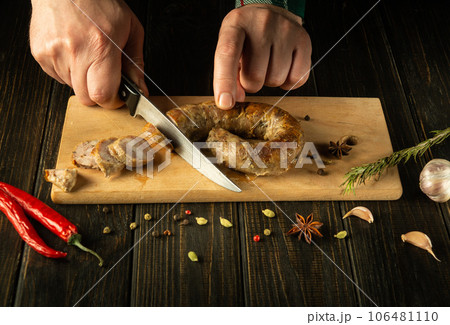 Close-up of the hands of the cook with a knife cut homemade fried sausage on a wooden board. Cooking a national meat dish at home 106481110