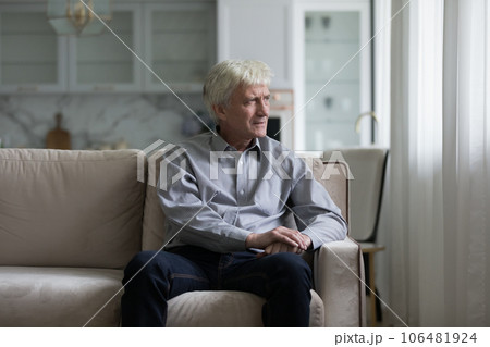 Serious concerned old retired man sitting on sofa, looking away 106481924