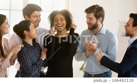 Smiling diverse colleagues greeting biracial coworker with work success 106482110