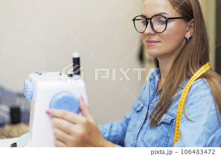 Beautiful young woman sewing clothes using a sewing machine Beautiful young woman sewing clothes using a sewing machine 106483472