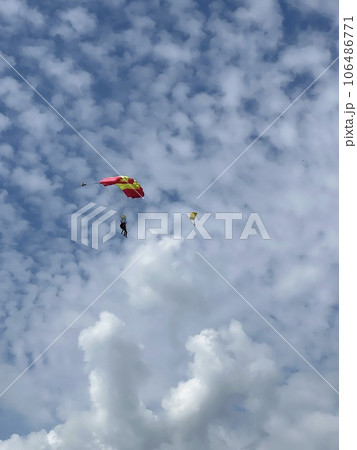Skydiver with a blue little canopy of a parachute on the background a blue sky and white clouds, close-up. Skydiver under parachute above the stormy clouds. Lithuania 106486771