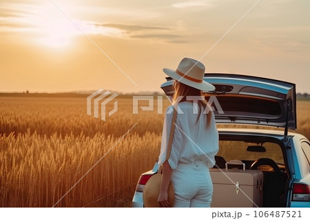 a woman standing next to her car in a wheat field at sunset with the sun shining through the back window a woman standing next to her car in a wheat field at sunset with the sun shining through the back window 106487521