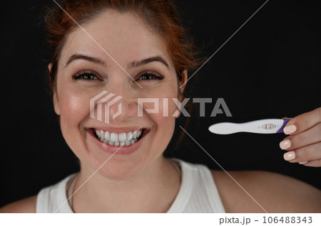 Portrait of happy caucasian woman holding positive express pregnancy test on black background. Portrait of happy caucasian woman holding positive express pregnancy test on black background. 106488343