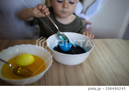 little cute boy paints eggs for easter sitting in the kitchen at the table 106490245