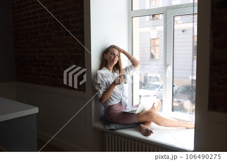 young beautiful woman drinking coffee sitting by the big window in the apartment 106490275