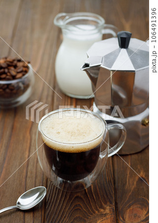 espresso in cup and geyser coffee maker and jug of cream on wooden table 106491396