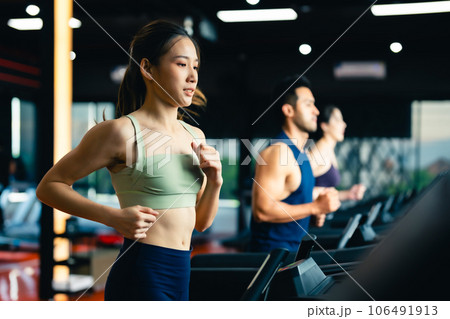 Fit young woman and man running on a treadmill during a workout class at fitness gym 106491913