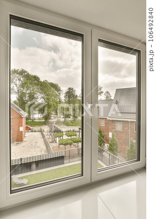an empty room with windows that look out onto the street, and houses are visible in the window panes 106492840