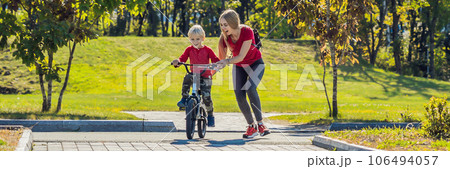 Young mother teaching her son how to ride a bicycle in the park BANNER, LONG FORMAT Young mother teaching her son how to ride a bicycle in the park BANNER, LONG FORMAT 106494057
