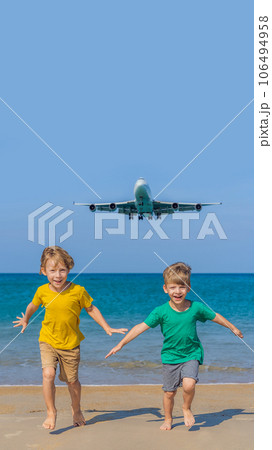 Two happy boys have fun on the beach watching the landing planes. Traveling on an airplane with kids concept. Text space. Island Phuket in Thailand. Impressive paradise. Hot beach Mai Khao. Amazing 106494958