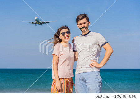 Man and woman tourists have fun on the beach watching the landing planes. Traveling on an airplane concept. Text space. Island Phuket in Thailand. Impressive paradise. Hot beach Mai Khao. Amazing 106494969
