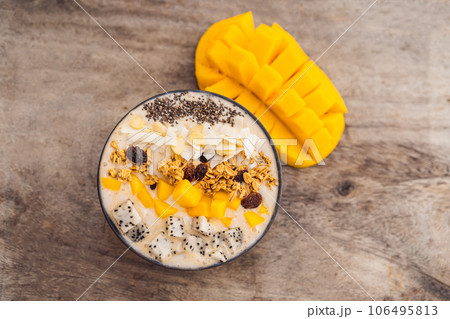 Smoothie bowls made with mango, banana, granola, grated coconut, dragon fruit, chia seeds and mint on wooden background. Concept fruits, vitamins Smoothie bowls made with mango, banana, granola, grated coconut, dragon fruit, chia seeds and mint on wooden background. Concept fruits, vitamins 106495813