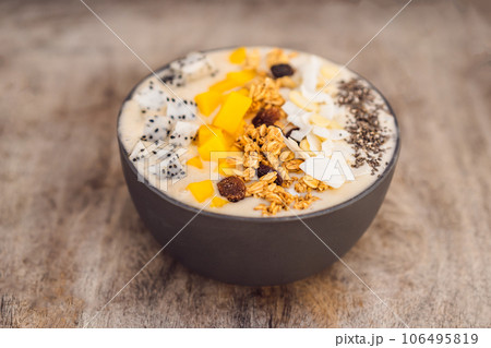 Smoothie bowls made with mango, banana, granola, grated coconut, dragon fruit, chia seeds and mint on wooden background. Concept fruits, vitamins 106495819