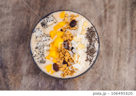 Smoothie bowls made with mango, banana, granola, grated coconut, dragon fruit, chia seeds and mint on wooden background. Concept fruits, vitamins 106495820