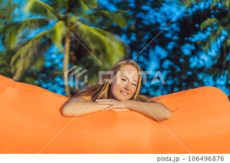 Summer lifestyle portrait of pretty girl sitting on the orange inflatable sofa on the beach of tropical island. Relaxing and enjoying life on air bed 106496876