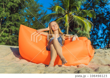 Summer lifestyle portrait of pretty girl sitting on the orange inflatable sofa on the beach of tropical island. Relaxing and enjoying life on air bed Summer lifestyle portrait of pretty girl sitting on the orange inflatable sofa on the beach of tropical island. Relaxing and enjoying life on air bed 106498123