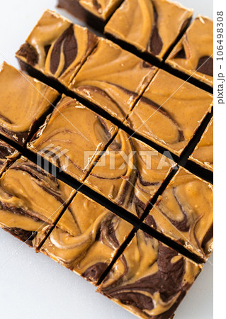 Cutting chocolate fudge with peanut butter swirl into small pieces on a white cutting board. Cutting chocolate fudge with peanut butter swirl into small pieces on a white cutting board. 106498308