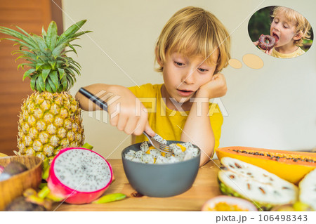 Boy eats fruit but dreams about donuts. Harmful and healthy food for children. Child eating healthy snack. Vegetarian nutrition for kids. Vitamins for children. Junk food concept 106498343