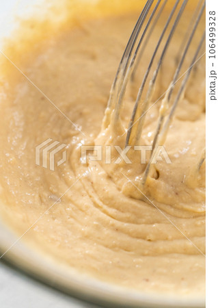 Mixing wet and dry ingredients with a hand whisk in a glass mixing bowl to prepare eggnog pancakes. 106499328