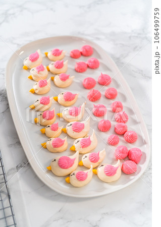 Decorating mini Easter bread kulich with sprinkles and meringue bird-shaped cookies. 106499759