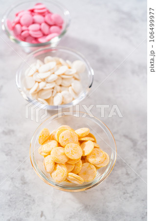 White, pink, and yellow chocolate chips in a small glass bowls on the kitchen counter. White, pink, and yellow chocolate chips in a small glass bowls on the kitchen counter. 106499977