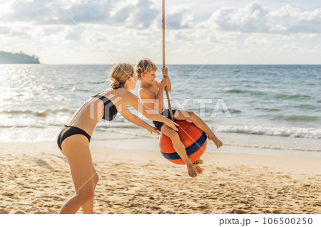 A boy on a swing on the beach. Mom and son spend time on the beach A boy on a swing on the beach. Mom and son spend time on the beach 106500250