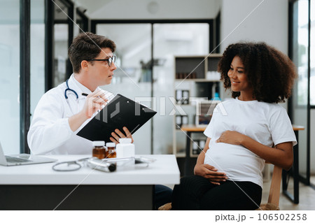 Pregnant african woman has appointment with doctor at clinic. Male gynaecologist OB GYN medic specialist with stethoscope listens to baby's heartbeat in mother's belly. Pregnancy, health care . Pregnant african woman has appointment with doctor at clinic. Male gynaecologist OB GYN medic specialist with stethoscope listens to baby's heartbeat in mother's belly. Pregnancy, health care . 106502258