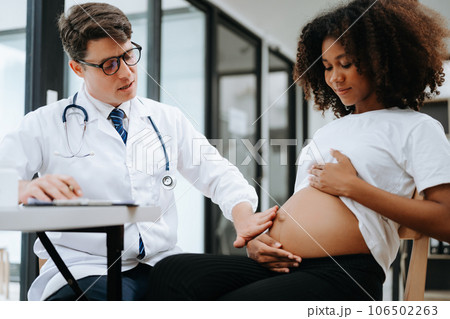 Pregnant african woman has appointment with doctor at clinic. Male gynaecologist OB GYN medic specialist with stethoscope listens to baby's heartbeat in mother's belly. Pregnancy, health care . 106502263