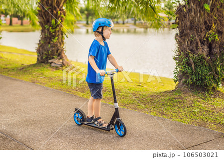 Boy riding scooters, outdoor in the park, summertime. Kids are happy playing outdoors Boy riding scooters, outdoor in the park, summertime. Kids are happy playing outdoors 106503021