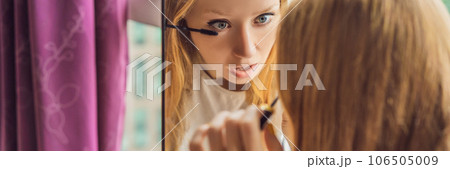 Young woman does makeup sitting by the window with a panoramic view of the skyscrapers and the big city BANNER, LONG FORMAT 106505009