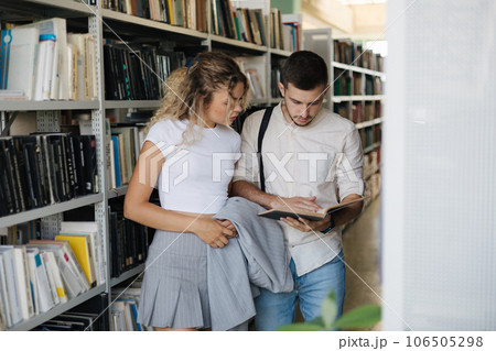 Handsome man and attractive female looking for book in university library. Woman show something to classmate in book 106505298
