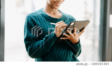 Beautiful Young African woman holding and using digital tablet while drinking coffee at home office and cafe 106505365