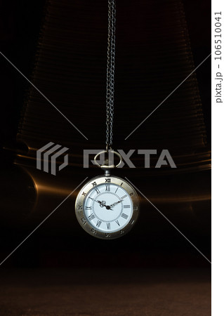Hypnosis session. Vintage pocket watch with chain swinging over surface on dark background among faded clock faces, magic motion effect 106510041