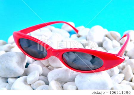 sunny stylish glasses in bright red rim white sea stones, blue background, concept sunny stylish glasses in bright red rim white sea stones, blue background, concept 106511390