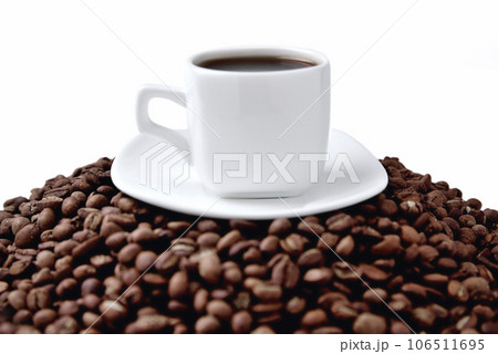 white cup of coffee on a white saucer stands on a hill of coffee beans on a white background white cup of coffee on a white saucer stands on a hill of coffee beans on a white background 106511695