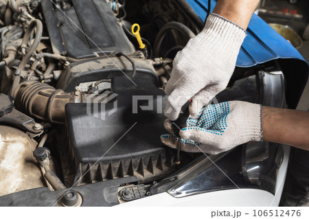 An auto mechanic unscrews the housing cover to replace the old engine air filter with a new one, is engaged in the maintenance of a passenger car An auto mechanic unscrews the housing cover to replace the old engine air filter with a new one, is engaged in the maintenance of a passenger car 106512476