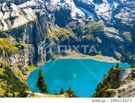 Oeschinensee lake with snow Bluemlisalp mountain on sunny summer day. Panorama of the azure lake Oeschinensee, pine forest in Swiss alps, Kandersteg. Switzerland. 106513871