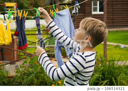 A happy caucasian 9 years boy helps her mother to hang up clothes. Development of fine motor skills through household activities. Selective focus. A happy caucasian 9 years boy helps her mother to hang up clothes. Development of fine motor skills through household activities. Selective focus. 106514321