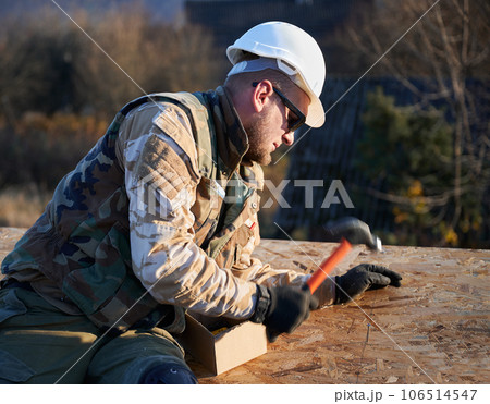Carpenter hammering nail into OSB panel on the roof top of future cottage. Man worker building wooden frame house. Carpentry and construction concept. 106514547