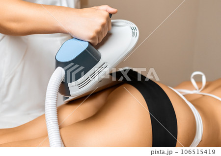 Specialist in a clinic office positions body sculpting equipment on the clients buttocks, initiating a procedure that promises visible improvements in appearance. 106515419