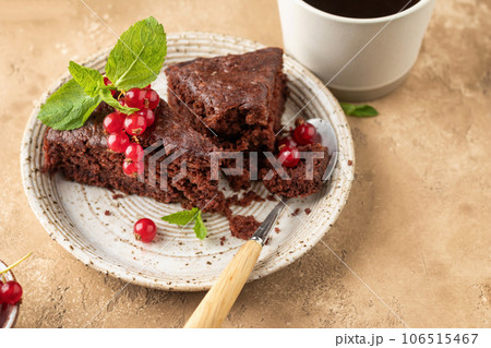 Two pieces of chocolate cake brownie close up decorated with red currant berries and mint for coffee on beige textured background 106515467