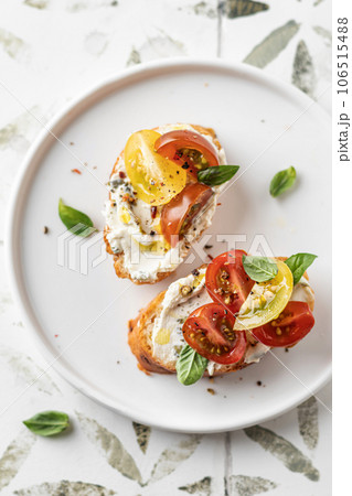 Bruschetta sandwiches with tomatoes, cream cheese, olive oil and basil on white plate on printed tile background close up, top view. Traditional italian antipasti 106515488