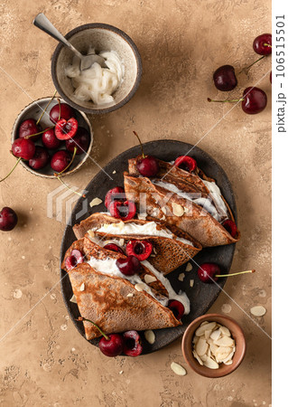 Chocolate crepes with cherry and whipped cream and almond petals on brown textured background rustic style top view, flat lay. Black forest recipe Chocolate crepes with cherry and whipped cream and almond petals on brown textured background rustic style top view, flat lay. Black forest recipe 106515501