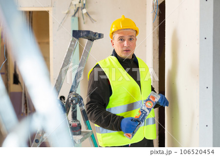 Builder in helmet is measuring wall with level closeup 106520454