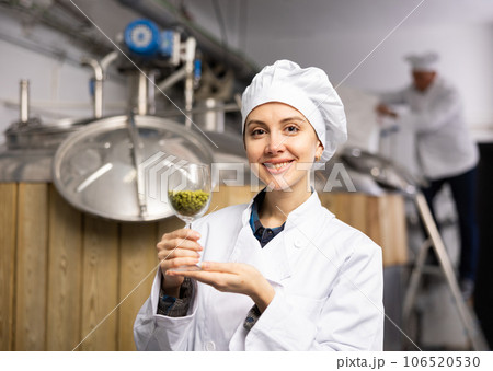 Portrait of a positive female brewer with a glass of hops at brewery 106520530
