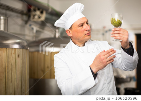 Brewer with glass filled with fresh hops at brewery 106520596