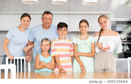 Happy dad and mum with three daughters and son is standing near kitchen table. 106520694
