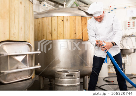 Brewmaster fixing hose pipe in workshop of beer factory 106520744