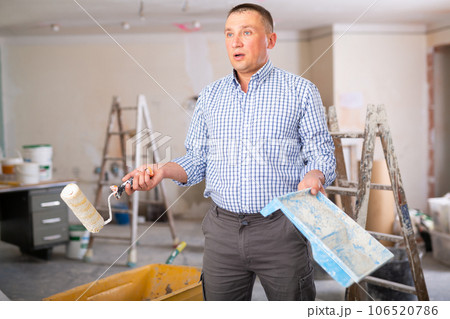 Portrait of confused man holding paint roller and tray, home improvement Portrait of confused man holding paint roller and tray, home improvement 106520786